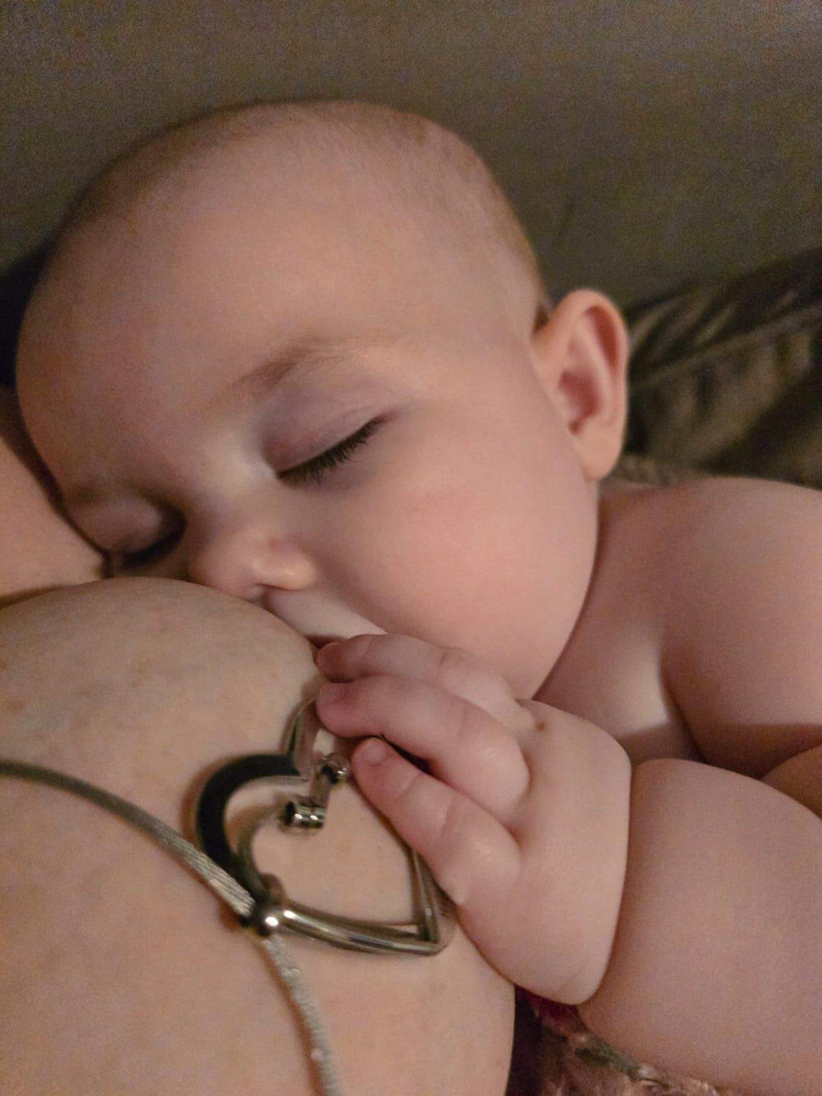 Baby holding a heart-shaped breastfeeding necklace close to its face